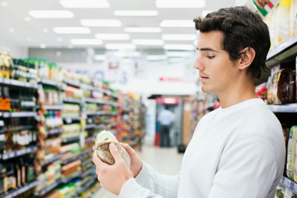 A young man reading the label on a food item in a supermarket